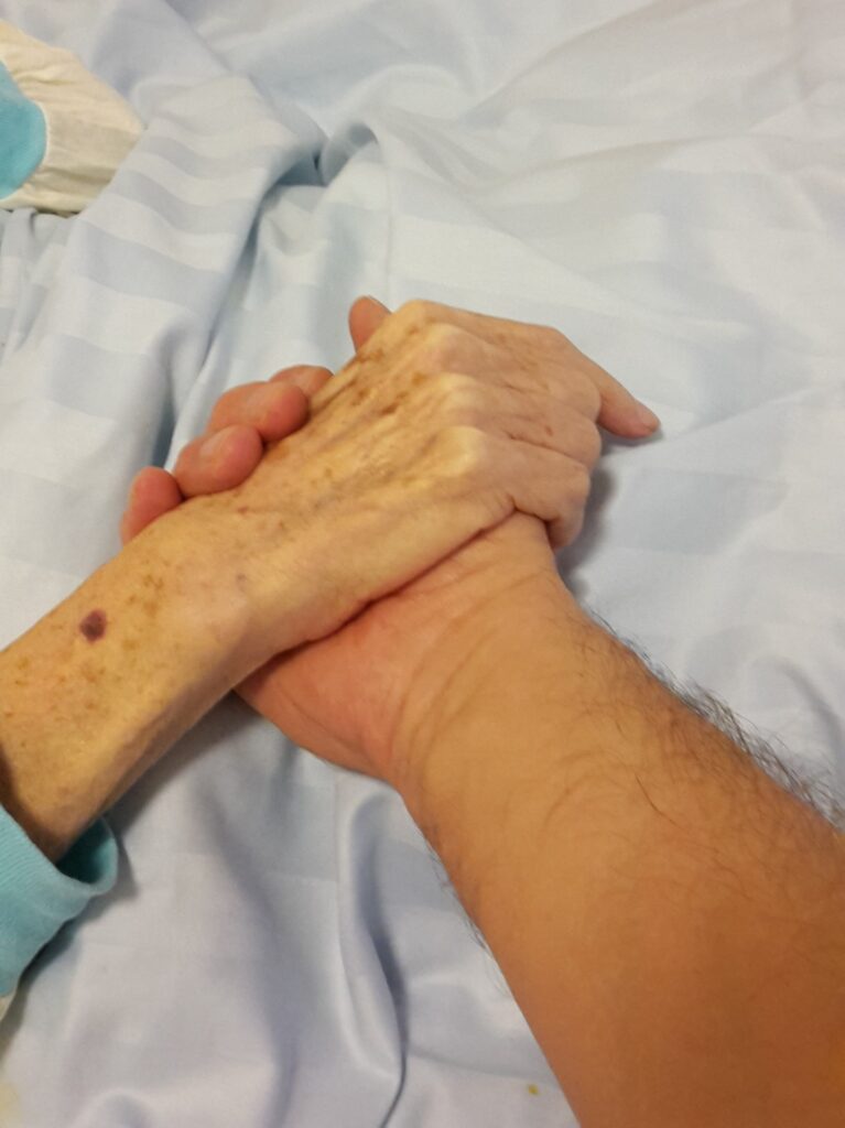 Un homme jeune tient la main d'un homme très âgé en service de soins palliatifs.